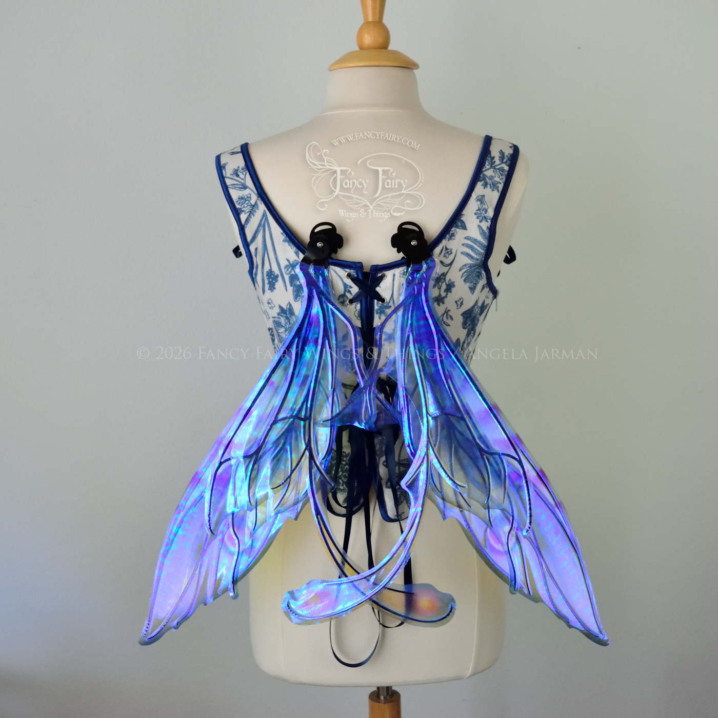Transparent iridescent blue, fuchsia and violet fairy wings with black veins, 3 panels on each side, bottom panels have tails that curve inward at the bottom. Worn on a dress form, back view, in resting position