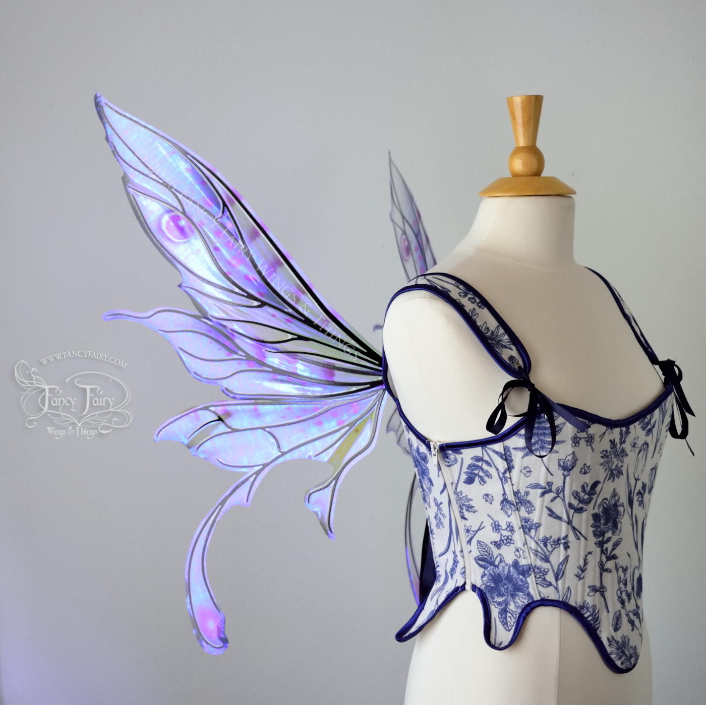 Transparent iridescent blue, fuchsia and violet fairy wings with black veins, 3 panels on each side, bottom panels have tails that curve inward at the bottom. Worn on a dress form, left side view