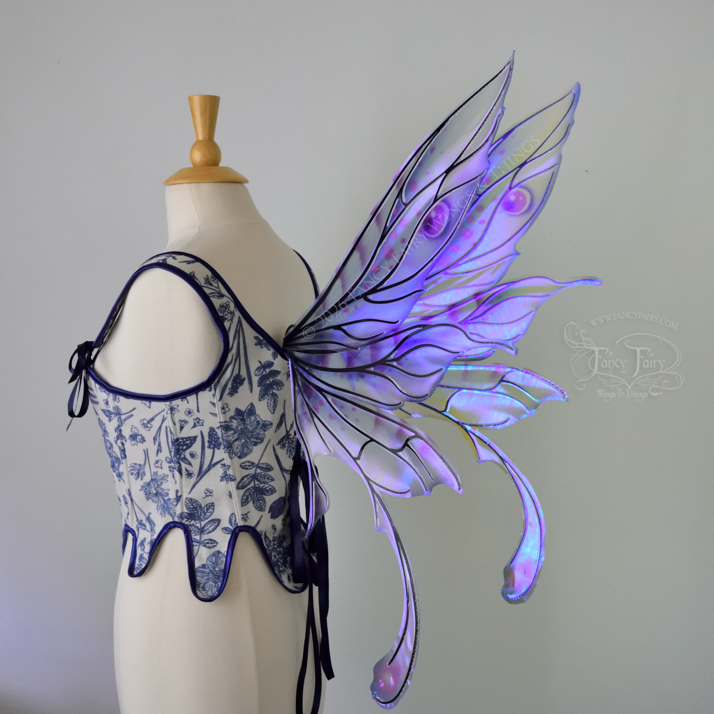 Transparent iridescent blue, fuchsia and violet fairy wings with black veins, 3 panels on each side, bottom panels have tails that curve inward at the bottom. Worn on a dress form, back 3/4 view