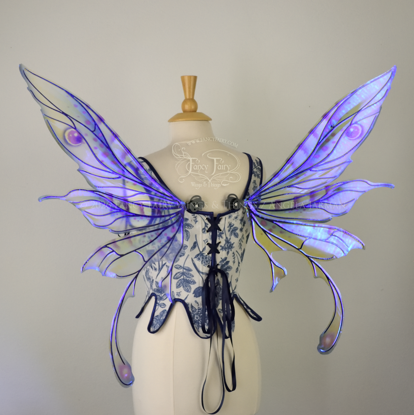 Transparent iridescent blue, fuchsia and violet fairy wings with black veins, 3 panels on each side, bottom panels have tails that curve inward at the bottom. Worn on a dress form, back view