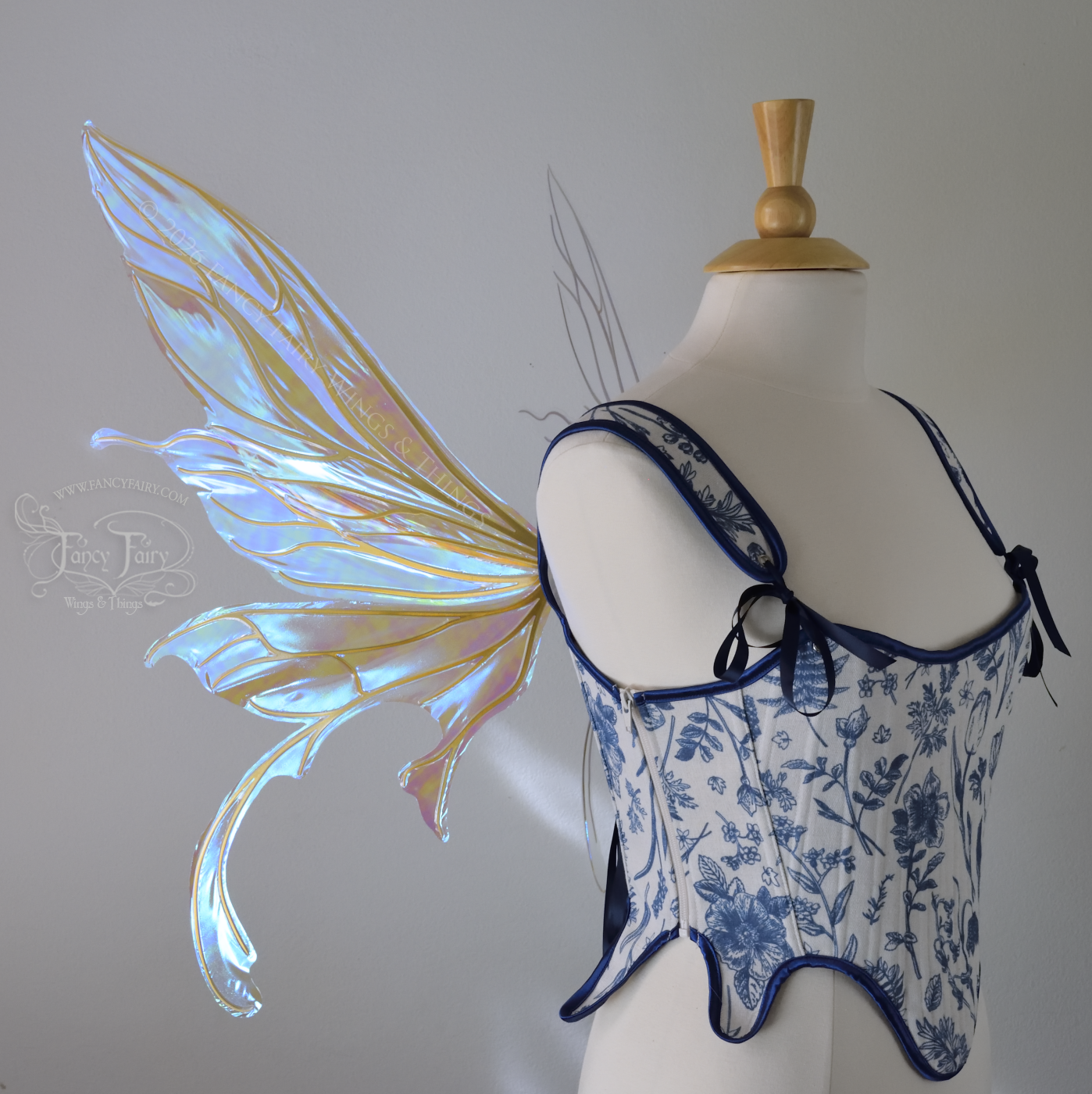Transparent iridescent blue fairy wings with gold veins, 3 panels on each side, bottom panels have tails that curve inward at the bottom. Worn on a dress form, left side view