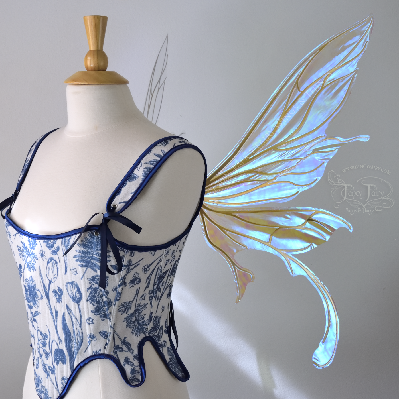 Transparent iridescent blue fairy wings with gold veins, 3 panels on each side, bottom panels have tails that curve inward at the bottom. Worn on a dress form, right side view