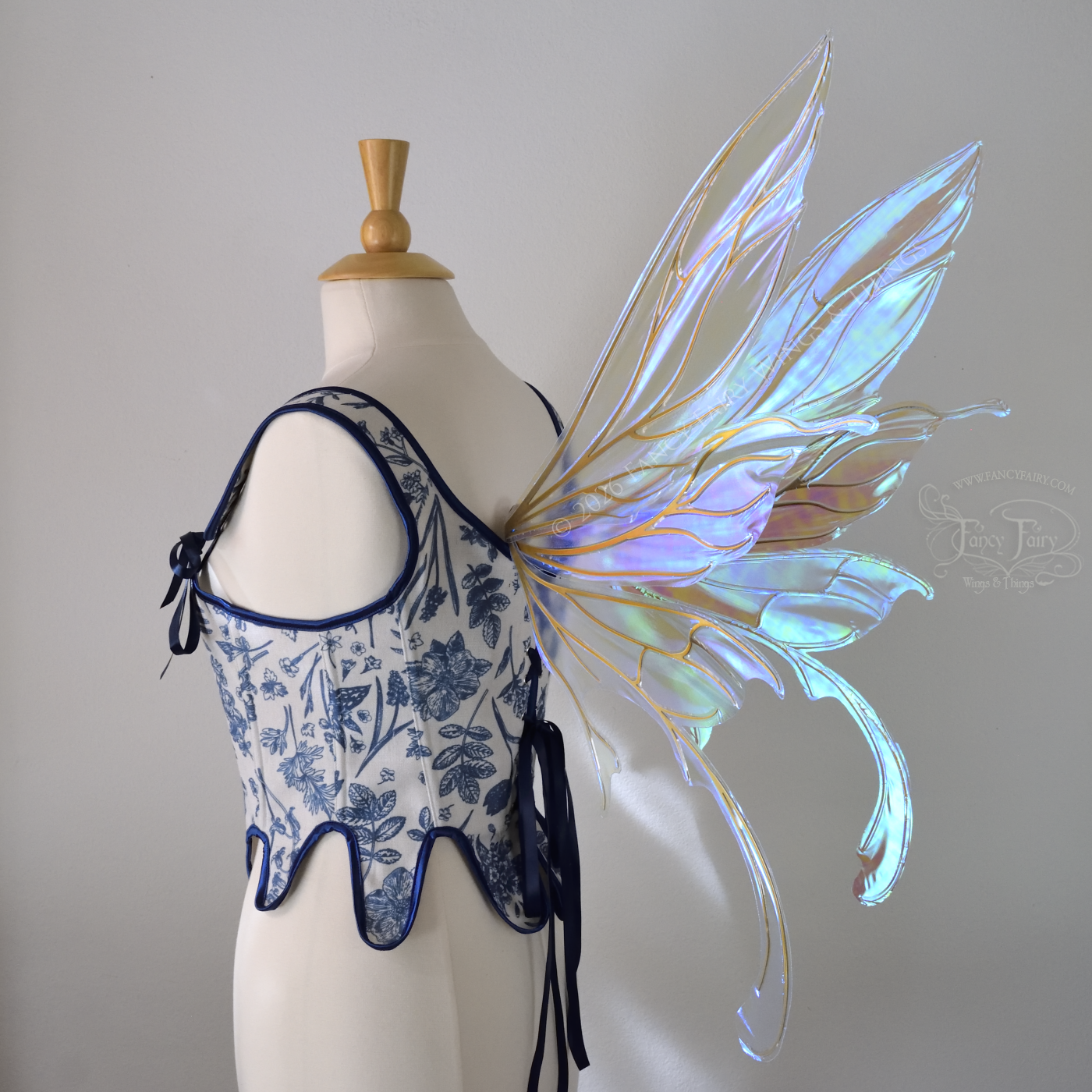 Transparent iridescent blue fairy wings with gold veins, 3 panels on each side, bottom panels have tails that curve inward at the bottom. Worn on a dress form, back 3/4 view