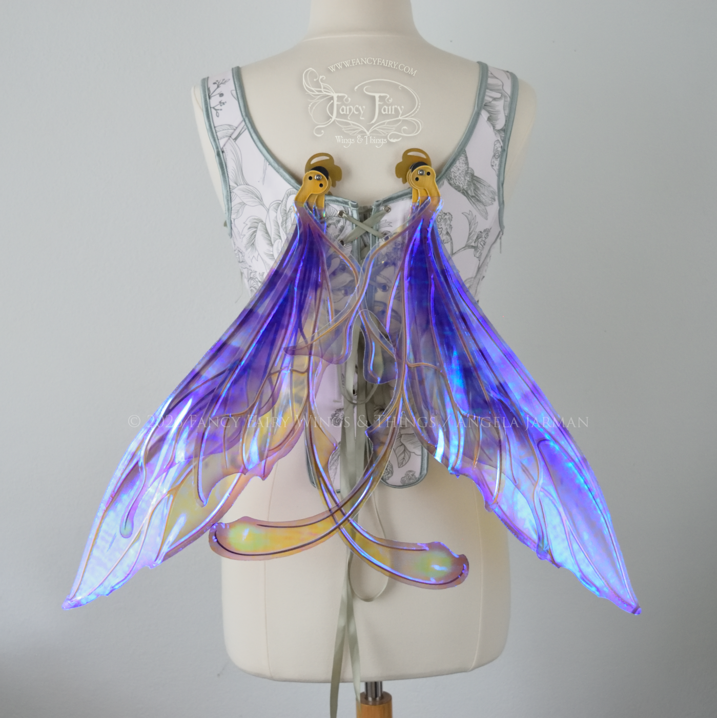 Transparent iridescent violet fairy wings with gold veins, 3 panels on each side, bottom panels have tails that curve inward at the bottom. Worn on a dress form, back view in resting position