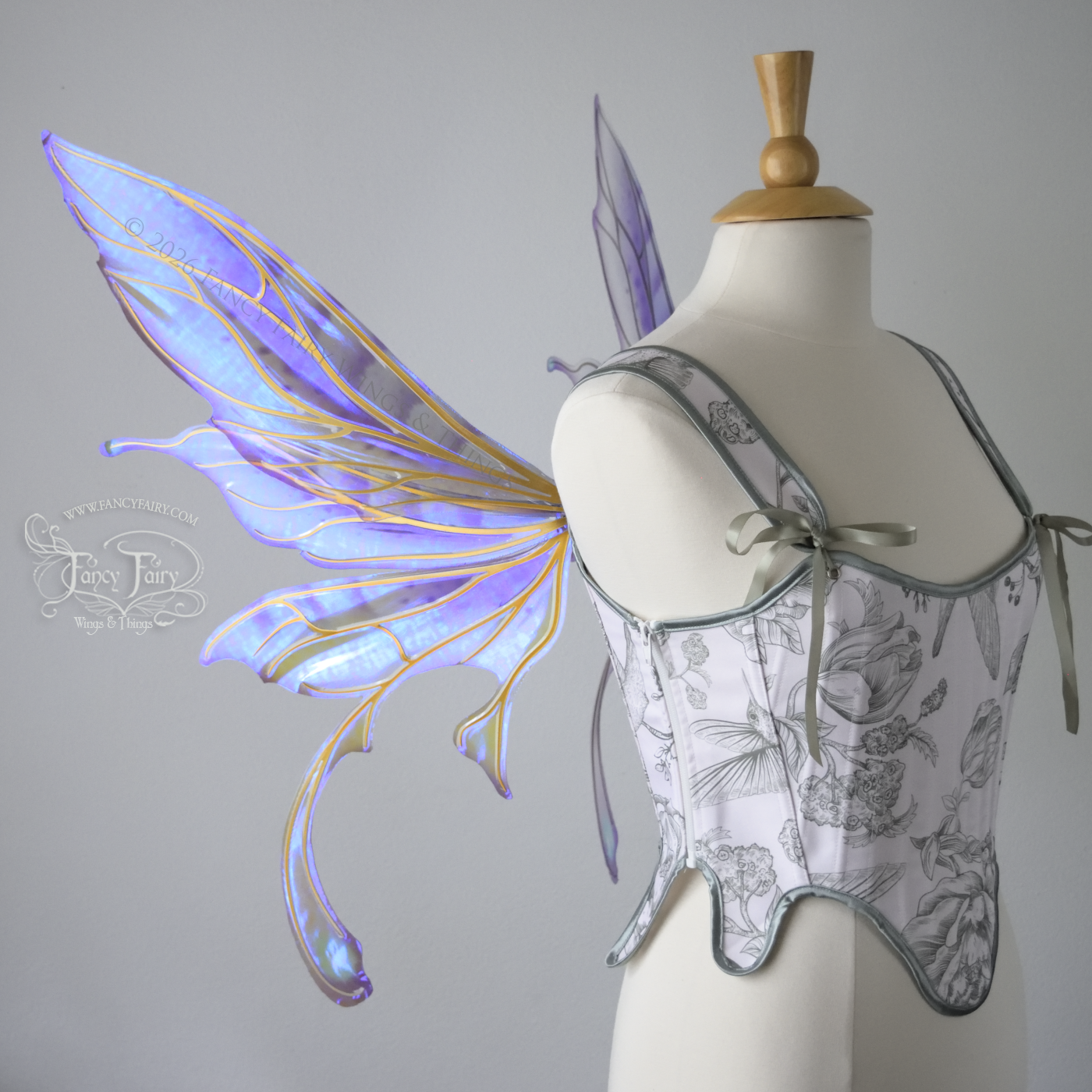 Transparent iridescent violet fairy wings with gold veins, 3 panels on each side, bottom panels have tails that curve inward at the bottom. Worn on a dress form, left side view