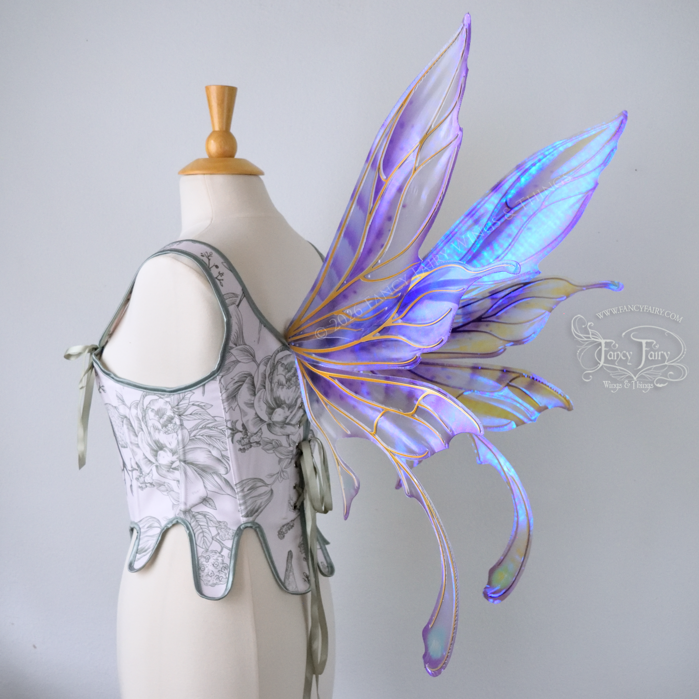 Transparent iridescent violet fairy wings with gold veins, 3 panels on each side, bottom panels have tails that curve inward at the bottom. Worn on a dress form, back 3/4 view