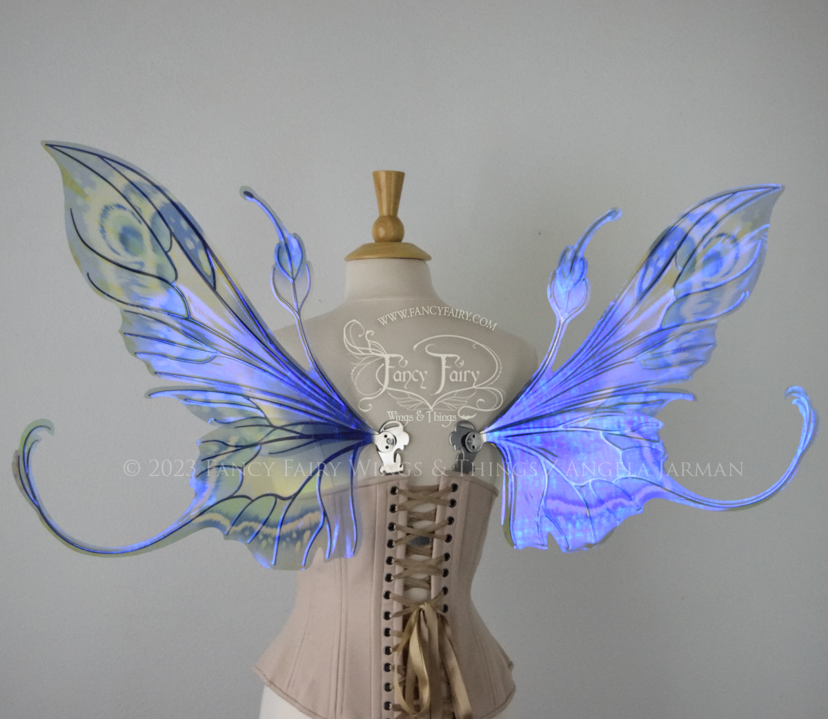 Back view of large blue, violet & teal painted iridescent fairy wings, elongated upper panels with antennae, bottom panels have a tail curving upwards, silver veins, worn on a dress form