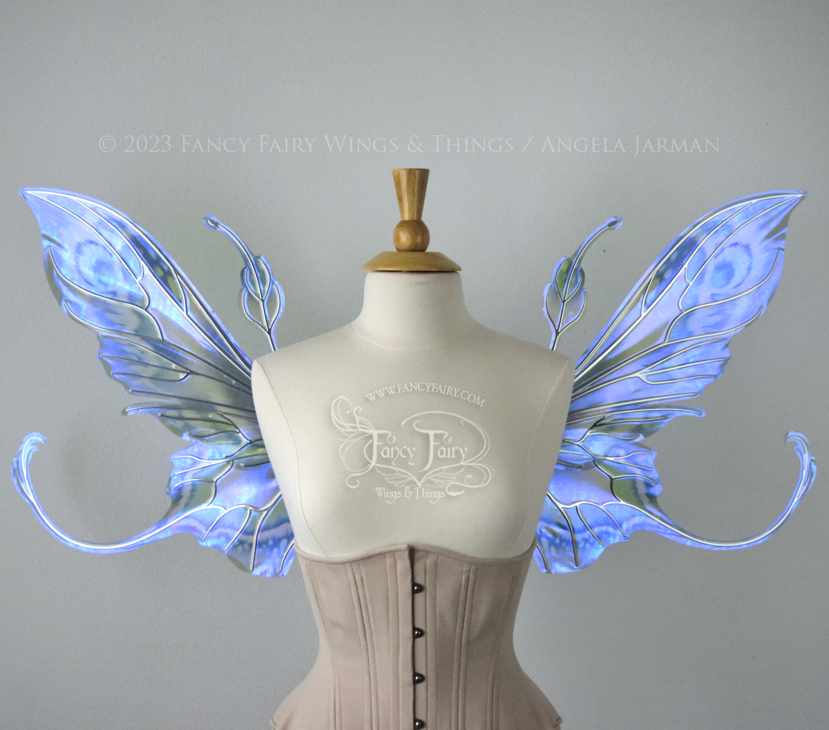 Front view of large blue, violet & teal painted iridescent fairy wings, elongated upper panels with antennae, bottom panels have a tail curving upwards, silver veins, worn on a dress form