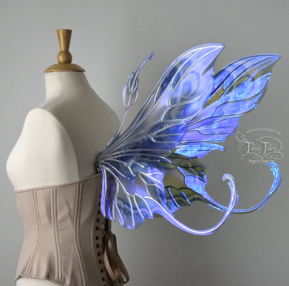 Back 3/4 view of large blue, violet & teal painted iridescent fairy wings, elongated upper panels with antennae, bottom panels have a tail curving upwards, silver veins, worn on a dress form
