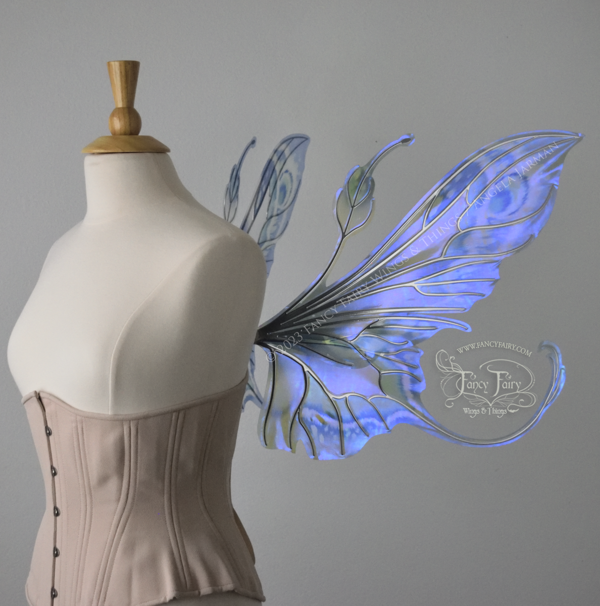 Right side view of large blue, violet & teal painted iridescent fairy wings, elongated upper panels with antennae, bottom panels have a tail curving upwards, silver veins, worn on a dress form