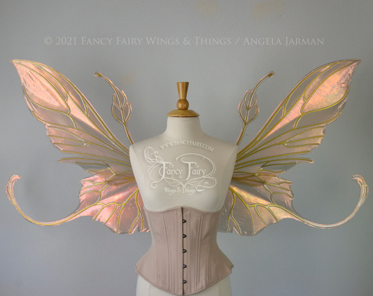 Front view of an ivory dress form wearing an alabaster underbust corset & extra large Rose Gold iridescent fairy wings with elongated upper panels & antennae with bottom panels that have a tail curving upwards, gold veins