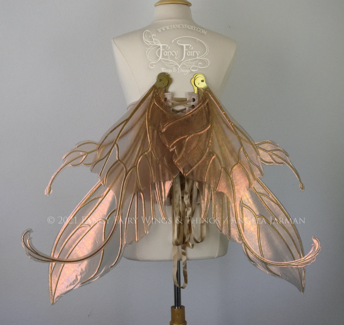 Back view of an ivory dress form wearing an alabaster underbust corset & extra large Rose Gold iridescent fairy wings with elongated upper panels & antennae with bottom panels that have a tail curving upwards, set in resting position, gold veins