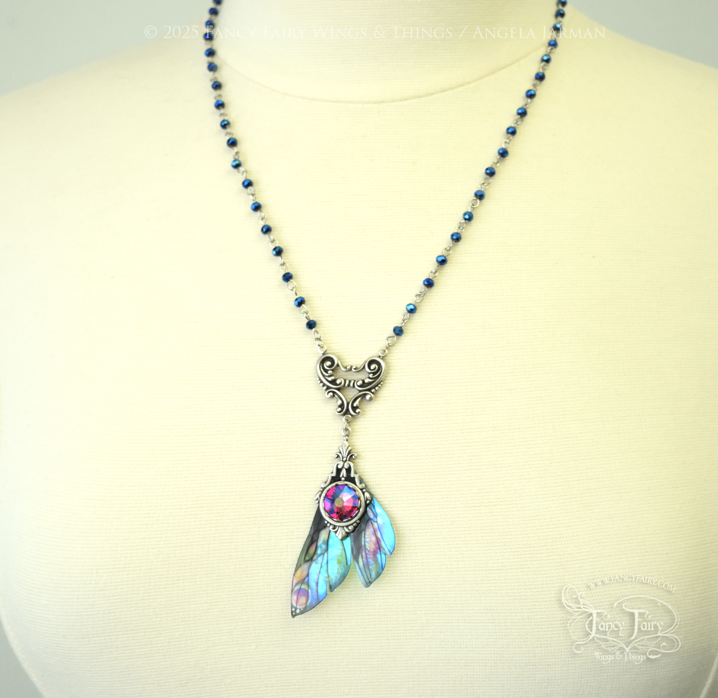 Iridescent fairy wing pendant necklace in teals with pink accents and silver filigree, hanging from a silver chain with blue faceted beads, worn on a dress form