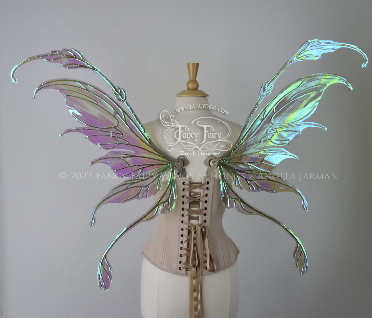 Back view of an ivory dress form wearing an alabaster underbust corset & large blue/green iridescent fairy wings with gold veins. The upper panels curve downward at top edge with antennae above, bottom panels have a narrow long tail