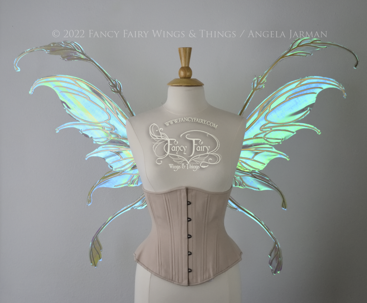 Front view of an ivory dress form wearing an alabaster underbust corset & large blue/green iridescent fairy wings with gold veins. The upper panels curve downward at top edge with antennae above, bottom panels have a narrow long tail