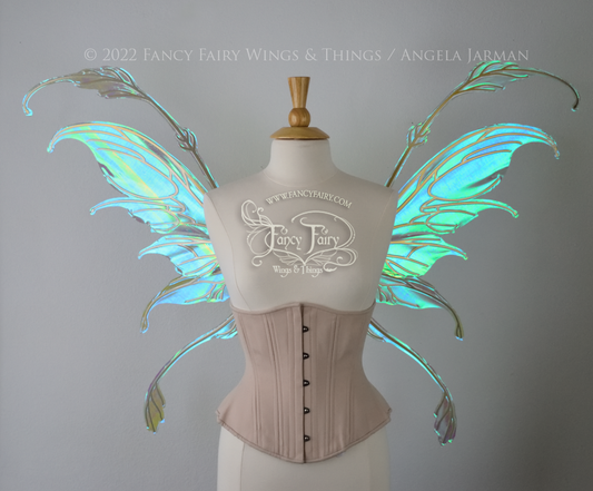 Front view of an ivory dress form wearing an alabaster underbust corset & large blue/green iridescent fairy wings with gold veins. The upper panels curve downward at top edge with antennae above, bottom panels have a narrow long tail