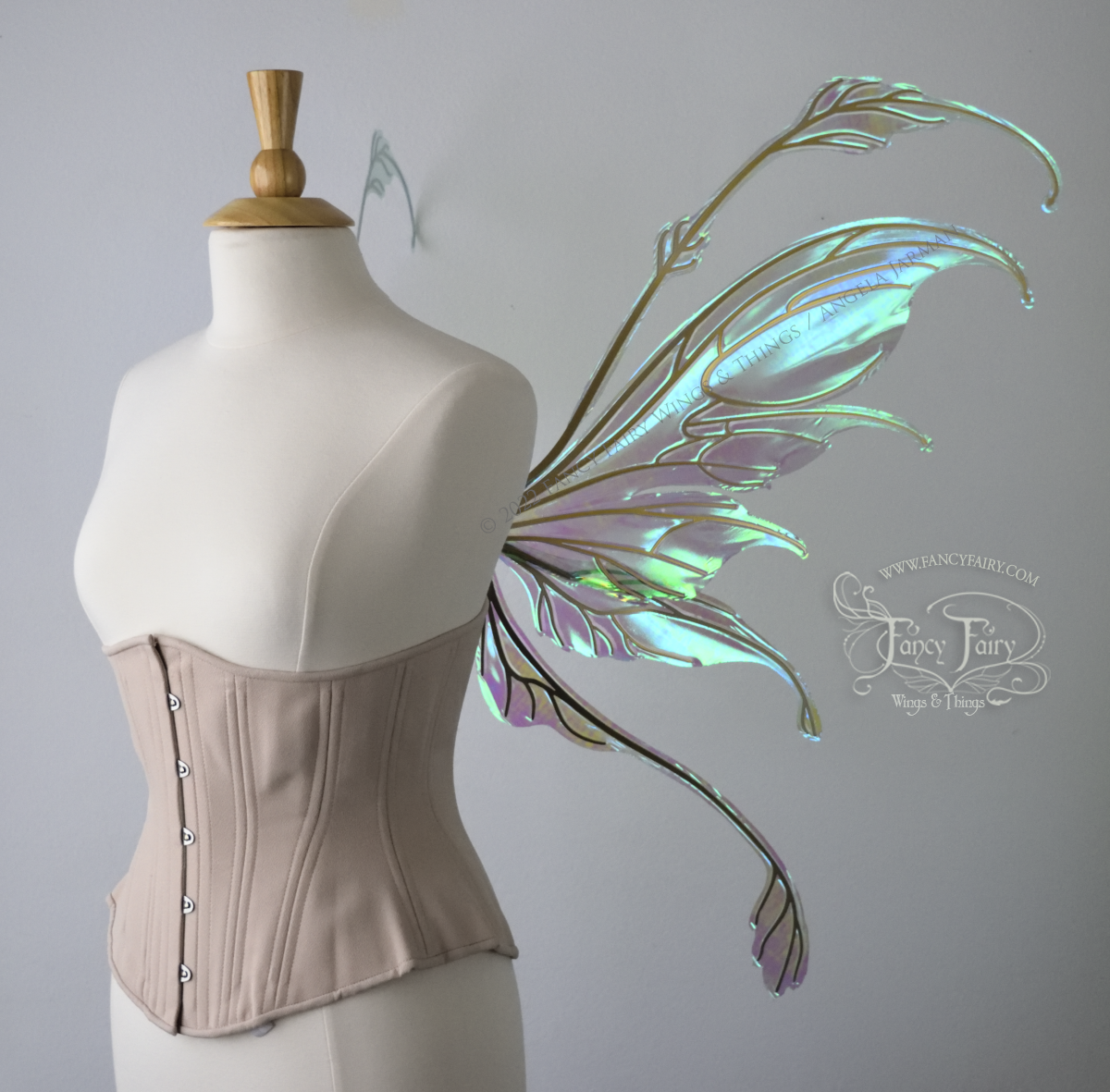 Right side view of an ivory dress form wearing an alabaster underbust corset & large blue/green iridescent fairy wings with gold veins. The upper panels curve downward at top edge with antennae above, bottom panels have a narrow long tail