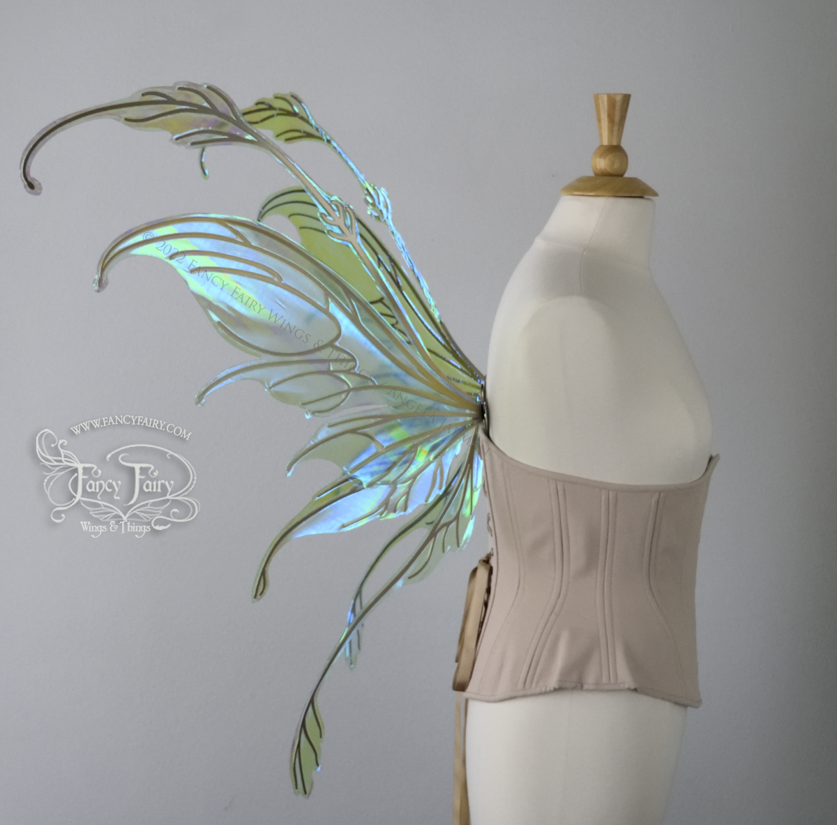 Left side view of an ivory dress form wearing an alabaster underbust corset & large blue/green iridescent fairy wings with gold veins. The upper panels curve downward at top edge with antennae above, bottom panels have a narrow long tail