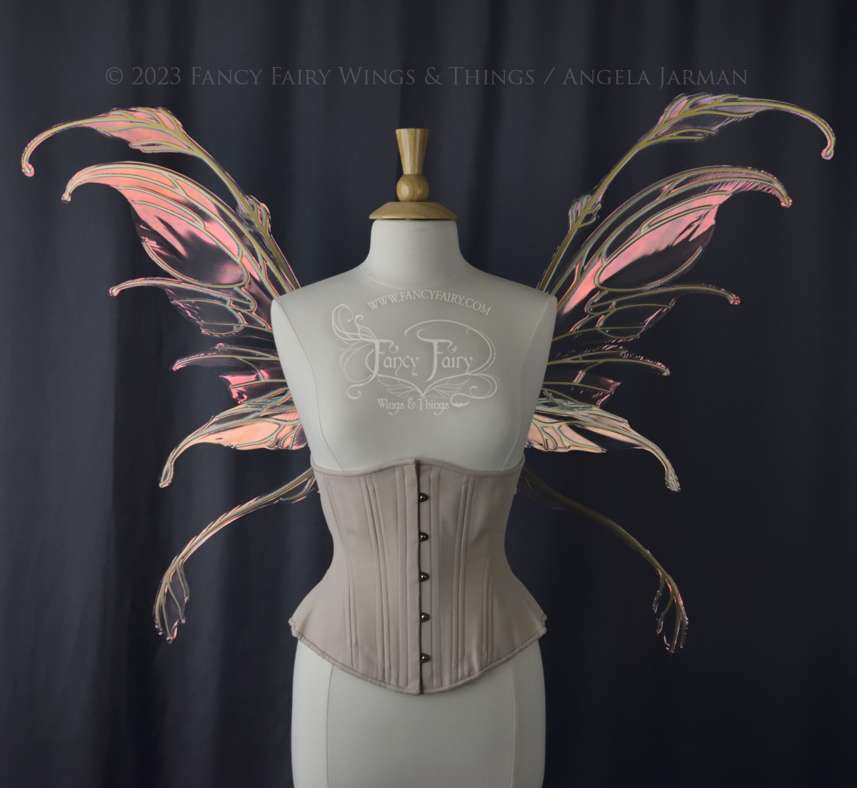 Front view of an ivory dress form wearing an underbust corset & 'Fauna' pinkish iridescent fairy wings with gold veining. Dark Grey background