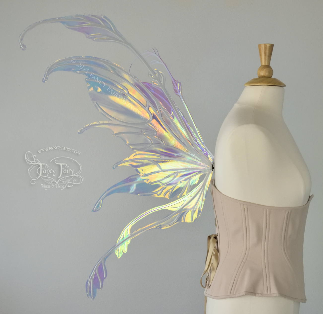 Left side view 2 of a dress form wearing an underbust corset & 'Fauna' transparent iridescent fairy wings with downward curved tips, antennae & wispy 'tails', with white veining