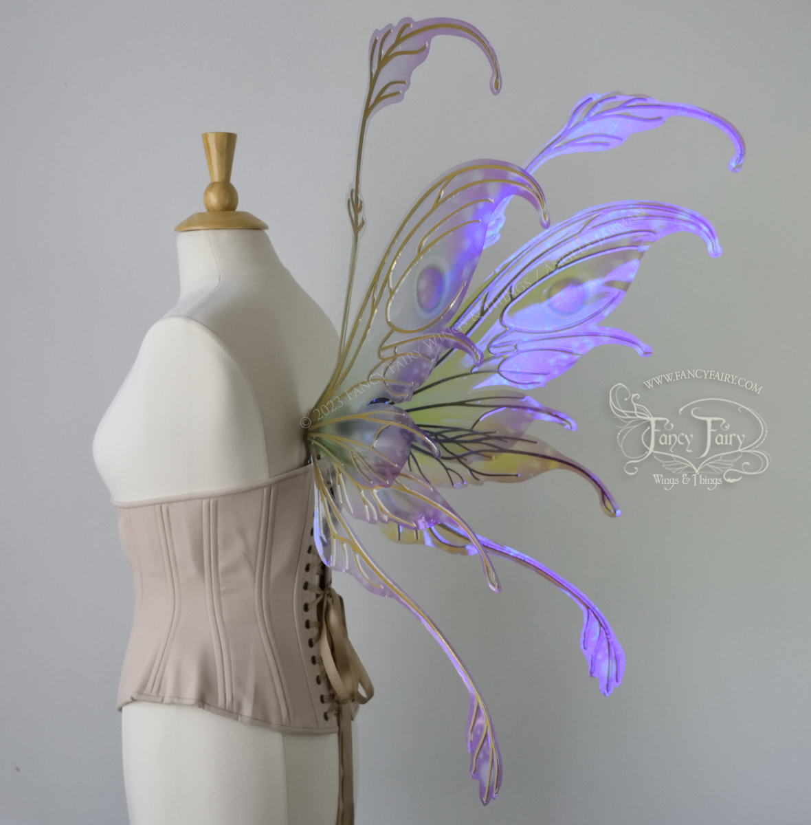 3/4 back view of a dress form wearing an underbust corset & 'Fauna' transparent pink, violet & green iridescent fairy wings with downward curved tips, antennae & wispy 'tails', with gold veining