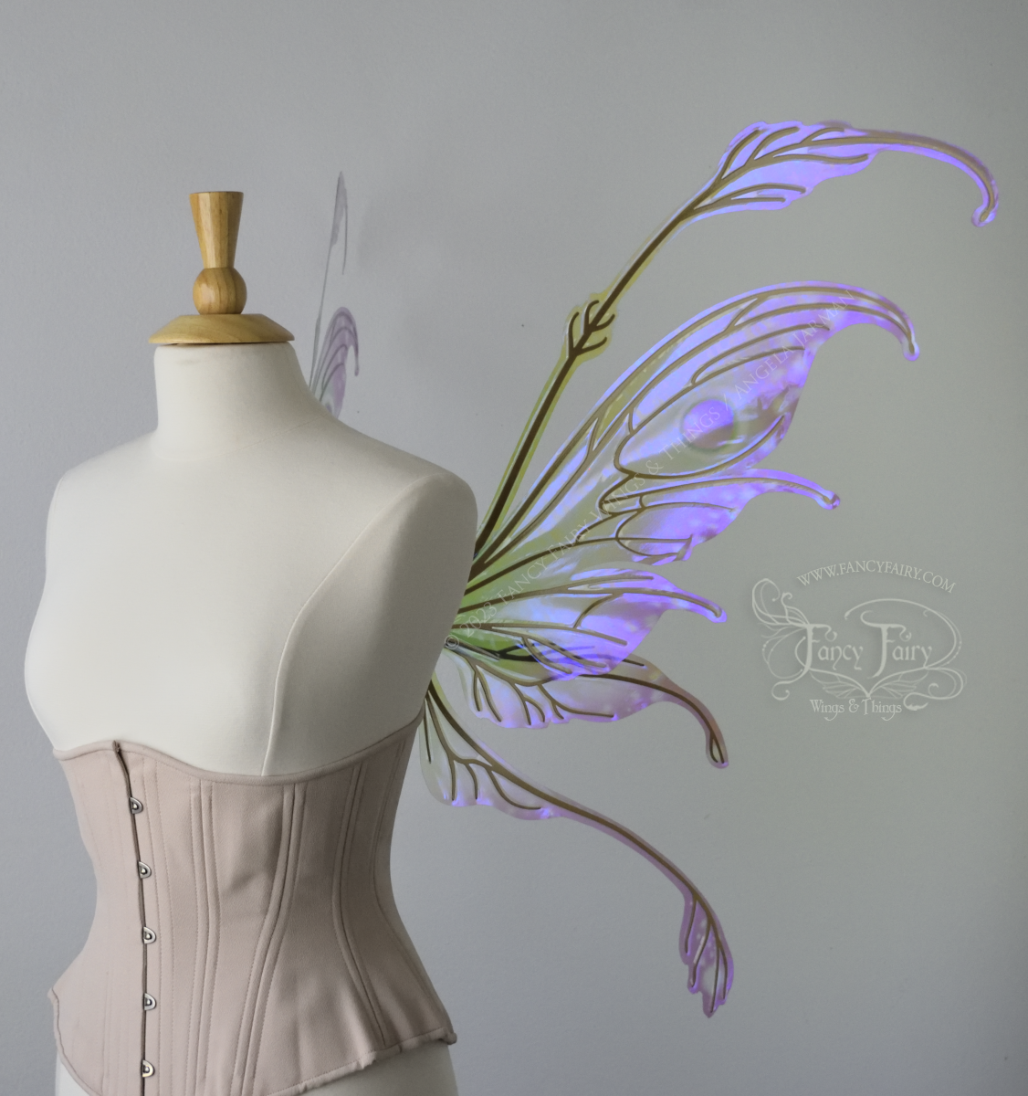 Right side view of a dress form wearing an underbust corset & 'Fauna' transparent pink, violet & green iridescent fairy wings with downward curved tips, antennae & wispy 'tails', with gold veining