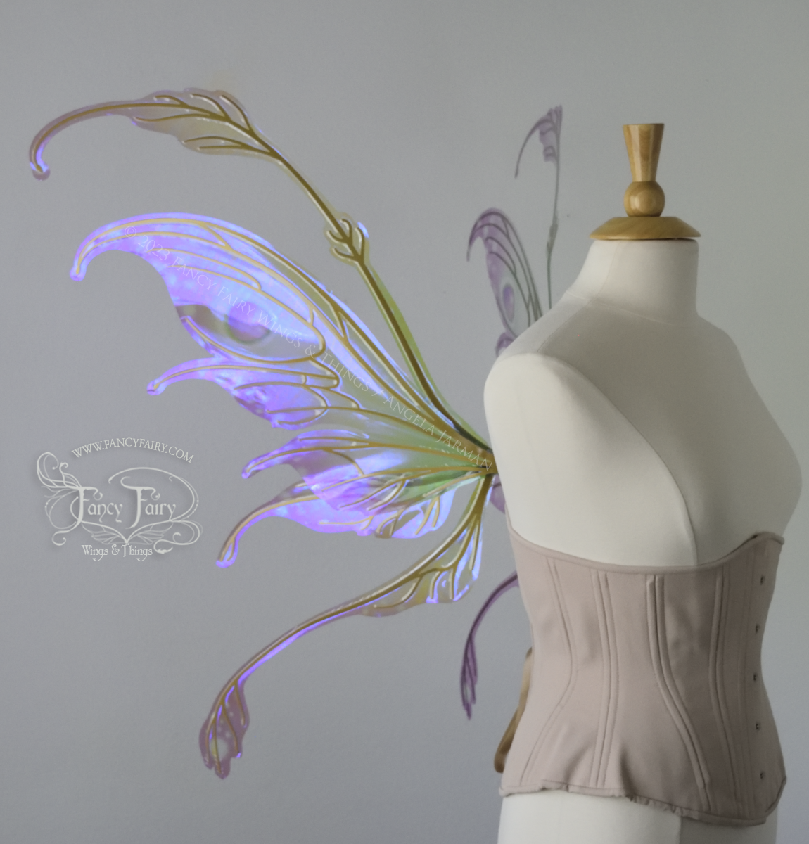 Left side view of a dress form wearing an underbust corset & 'Fauna' transparent pink, violet & green iridescent fairy wings with downward curved tips, antennae & wispy 'tails', with gold veining