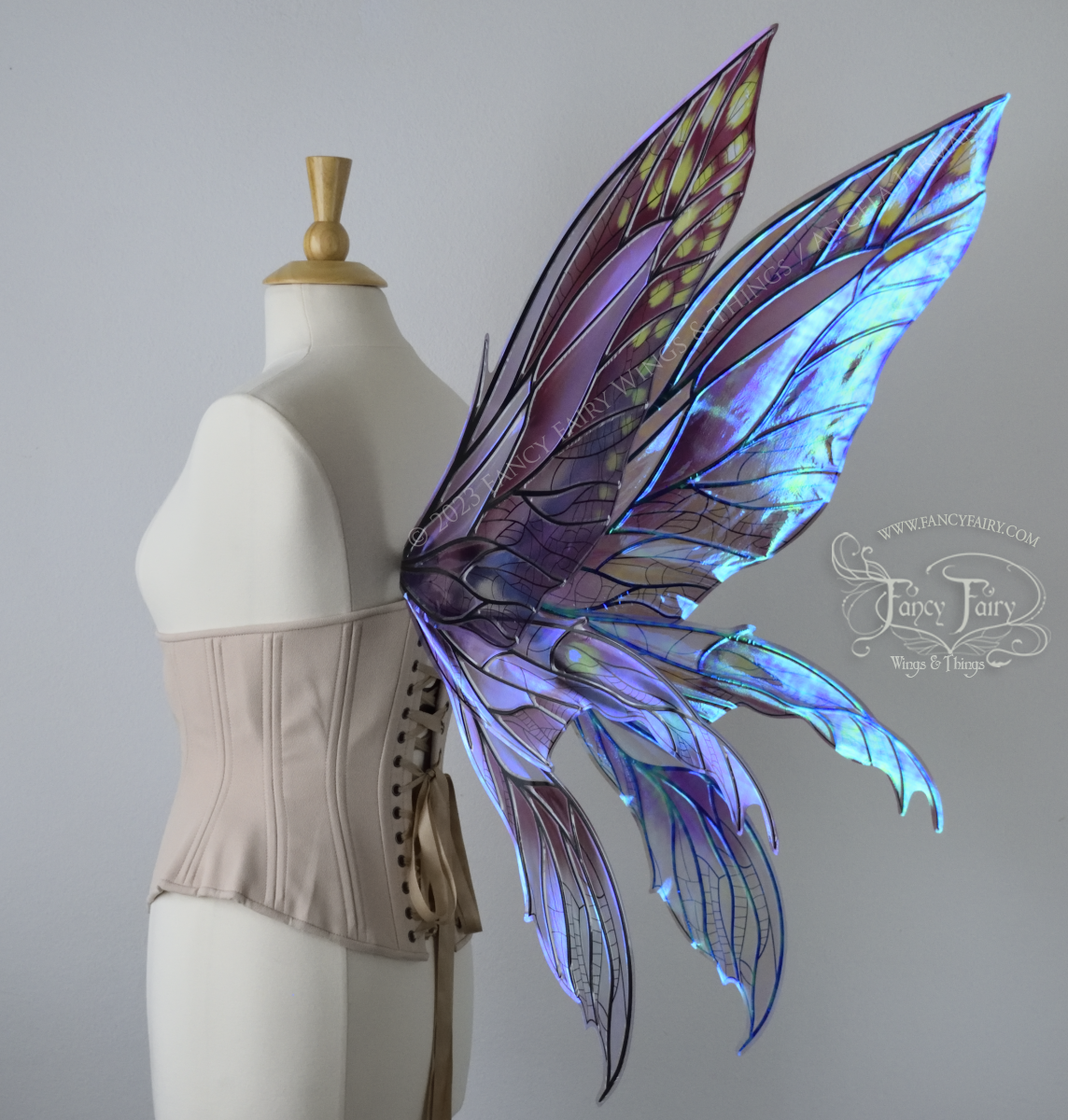 Back 3/4 view of dress form wearing large plum iridescent fairy wings with green accents. 3 pointed panels each side, detailed black veins
