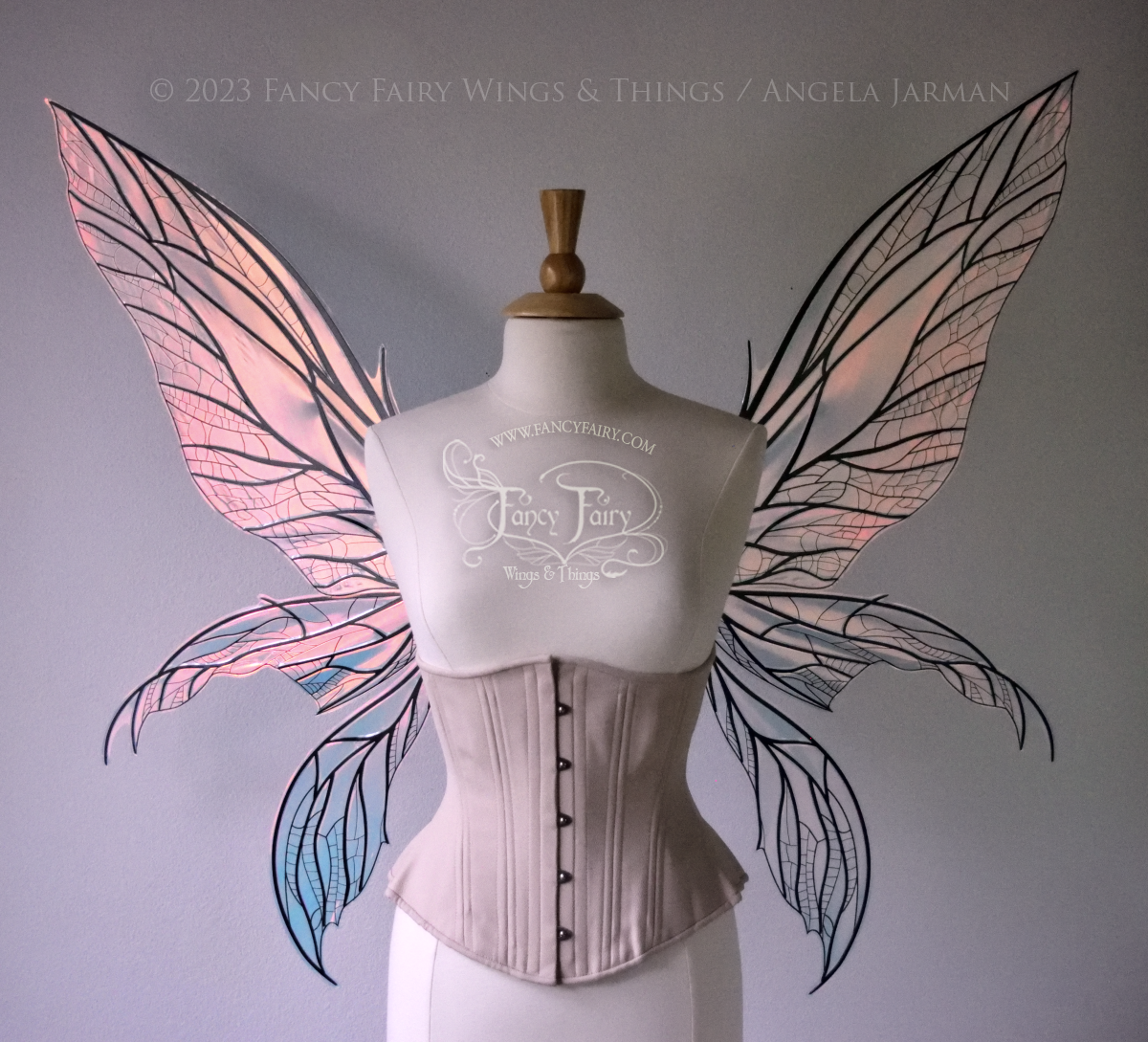 Front view of an ivory dress form wearing an alabaster underbust corset and large Blush iridescent fairy wings. Upper panels are elongated with pointed tips, 2 lower panels curve downward, lots of thin vein detail