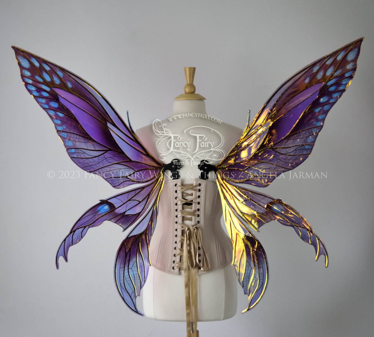 Back view of an ivory dress form wearing an alabaster underbust corset and large multicolor iridescent fairy wings. Upper panels are elongated with pointed tips, 2 lower panels curve downward, lots of thin vein detail