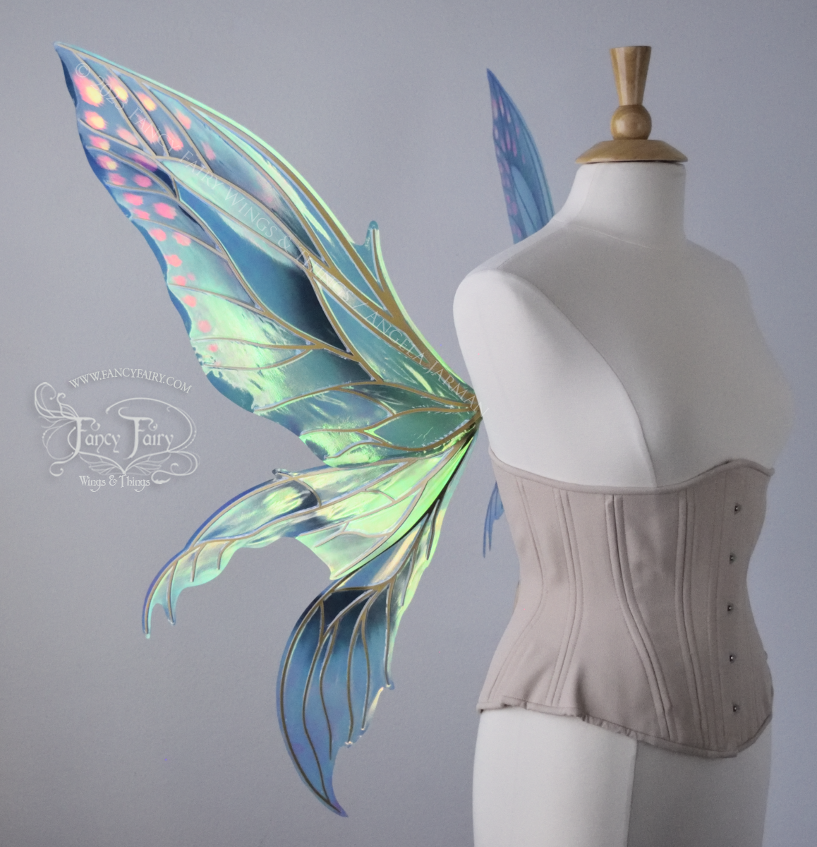 Left side view of large fairy wings in iridescent green and blue with pink spots near the tips of the upper panels, with gold veins, worn on a dressform