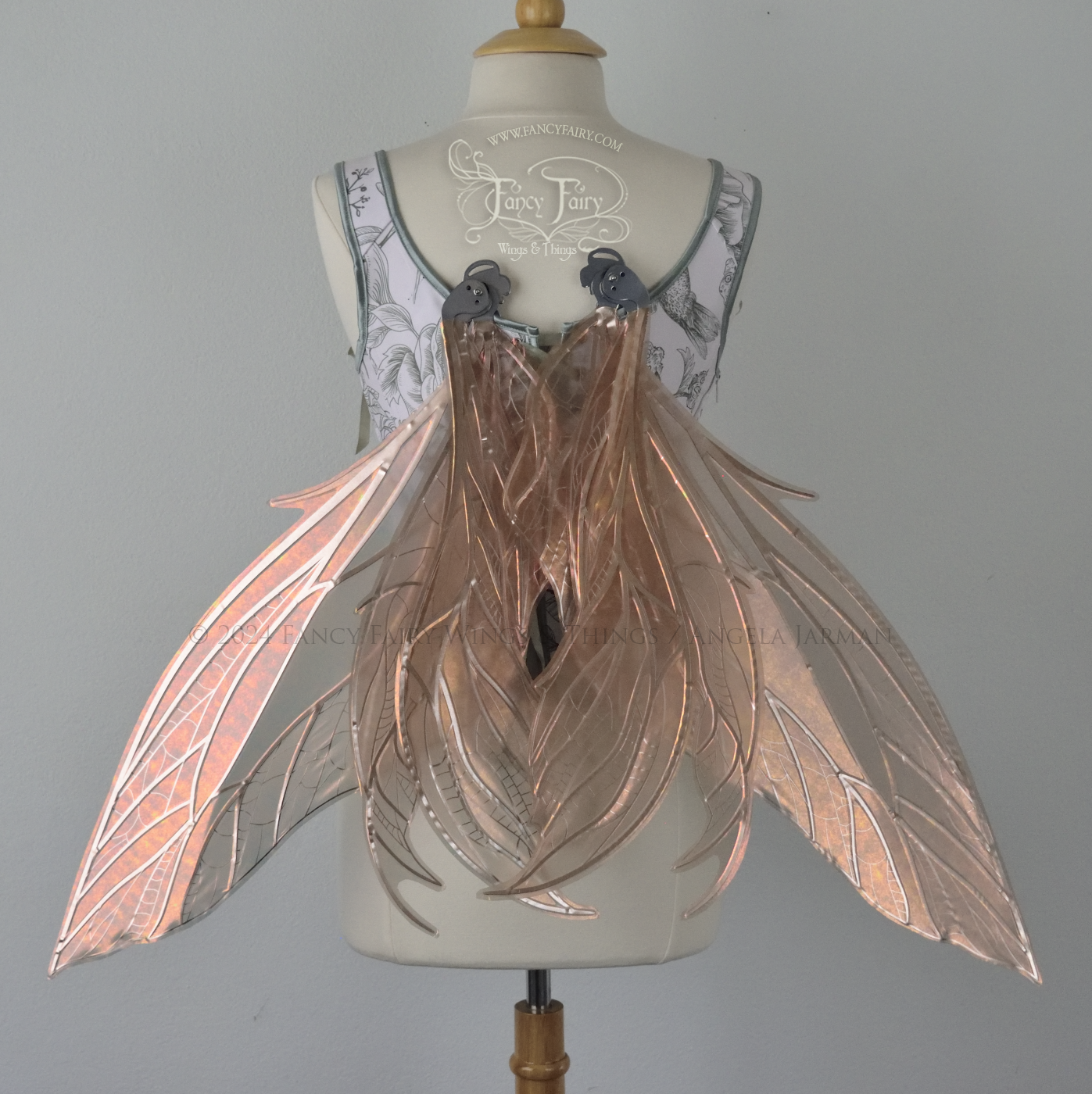 Large rose gold iridescent fairy wings with pointed tips & silver veins worn on a dress form with a white & green corset, back view, in resting position