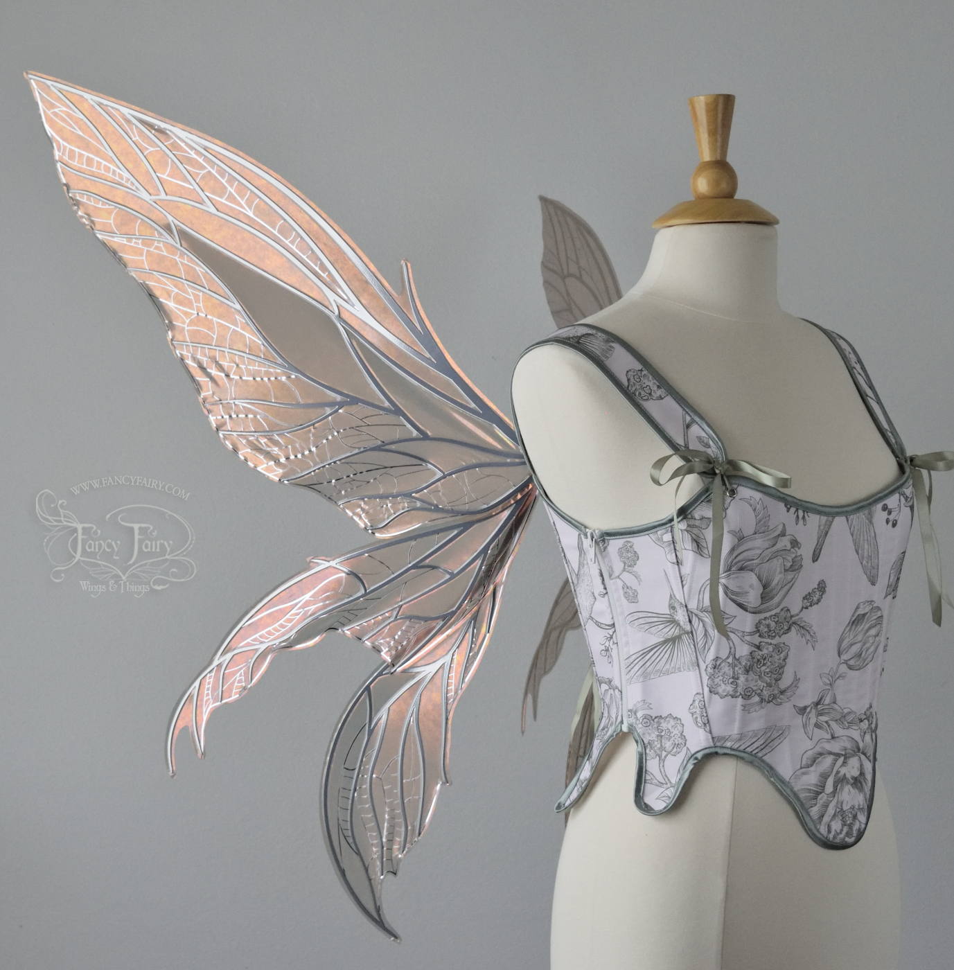 Large rose gold iridescent fairy wings with pointed tips & silver veins worn on a dress form with a white & green corset, left side view