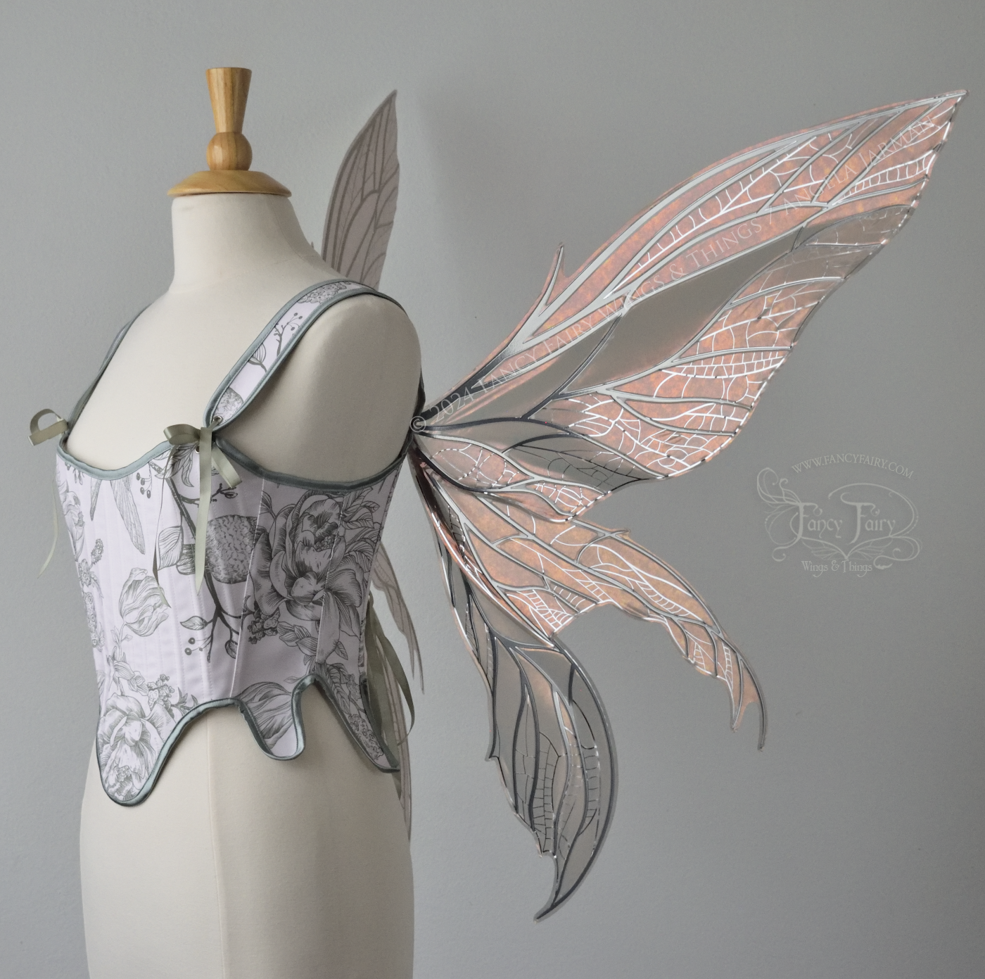 Large rose gold iridescent fairy wings with pointed tips & silver veins worn on a dress form with a white & green corset, right side view