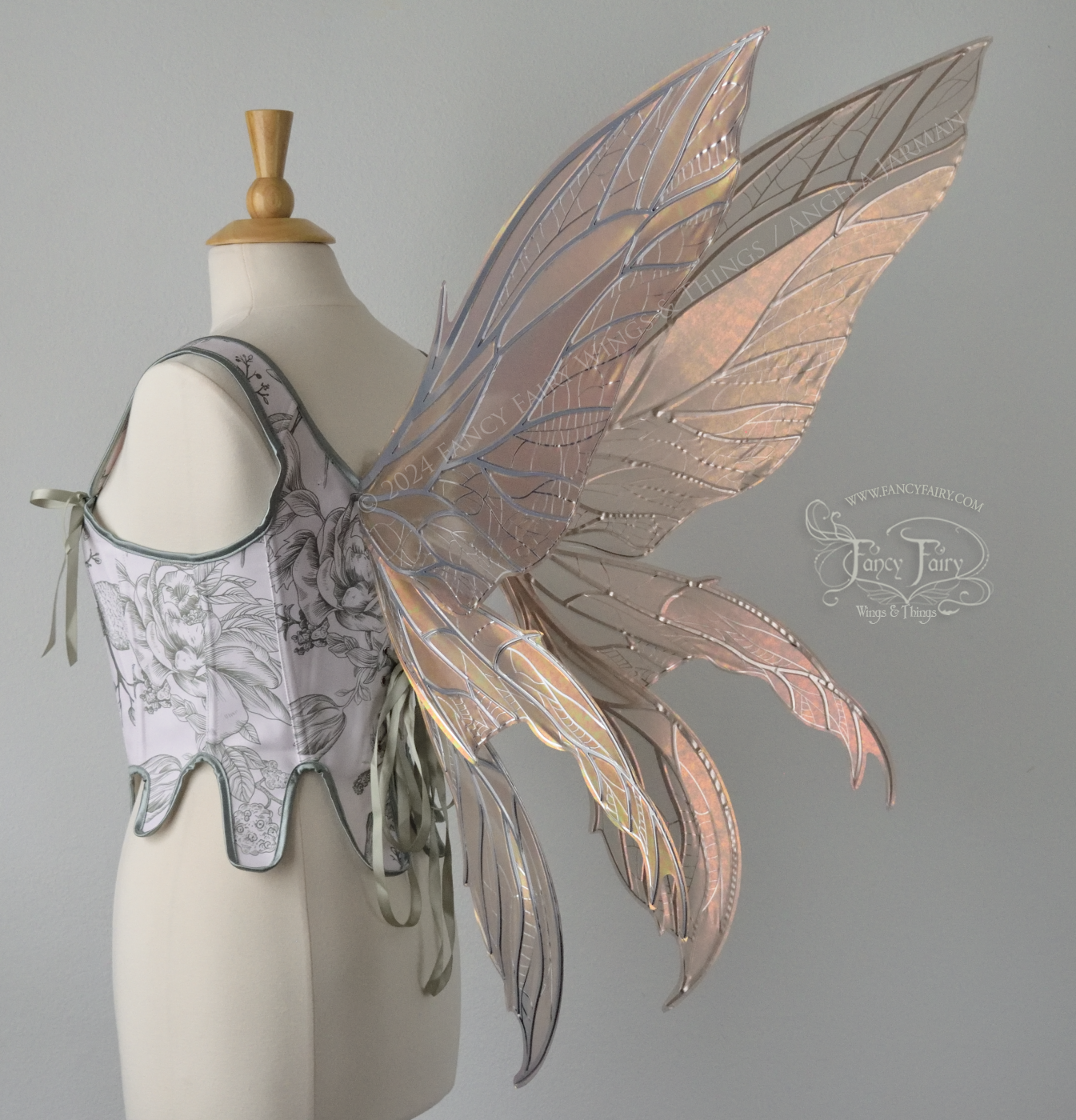 Large rose gold iridescent fairy wings with pointed tips & silver veins worn on a dress form with a white & green corset, back 3/4 view