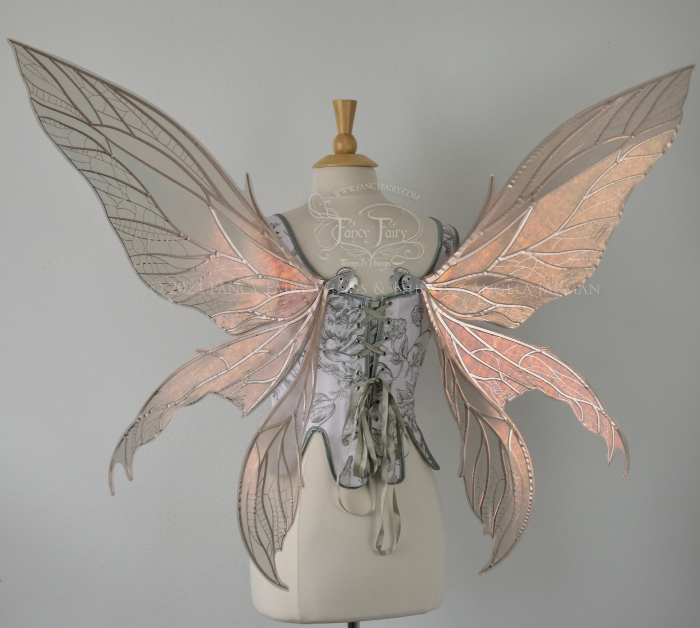 Large rose gold iridescent fairy wings with pointed tips & silver veins worn on a dress form with a white & green corset, back view