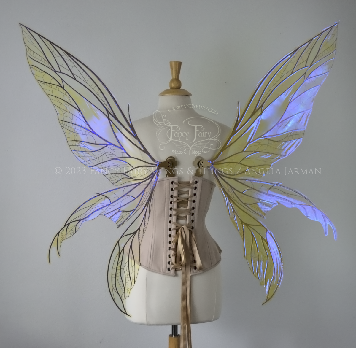 Back view of an ivory dress form wearing an alabaster underbust corset & large violet iridescent fairy wings. Upper panels are elongated with pointed tips, 2 lower panels curve downward, lots of thin vein detail in gold