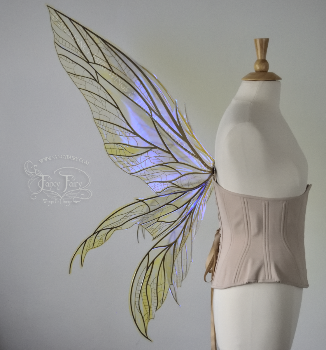 Left side view #2 of an ivory dress form wearing an alabaster underbust corset & large violet iridescent fairy wings. Upper panels are elongated with pointed tips, 2 lower panels curve downward, lots of thin vein detail in gold