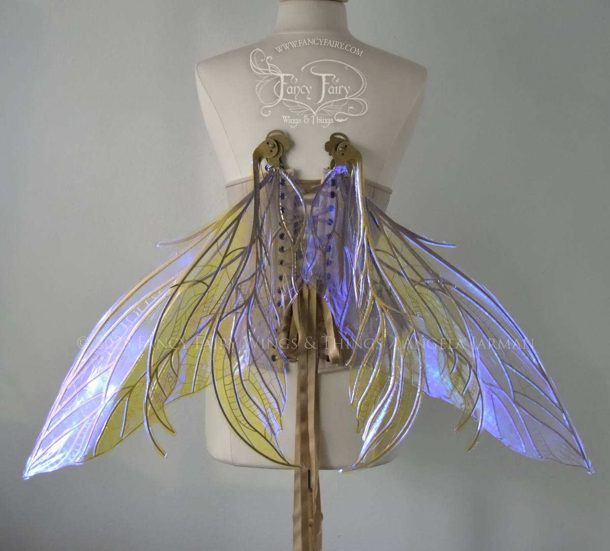 Back view of an ivory dress form wearing an alabaster underbust corset & large violet iridescent fairy wings. Upper panels are elongated with pointed tips, 2 lower panels curve downward, lots of thin vein detail in gold, in resting position