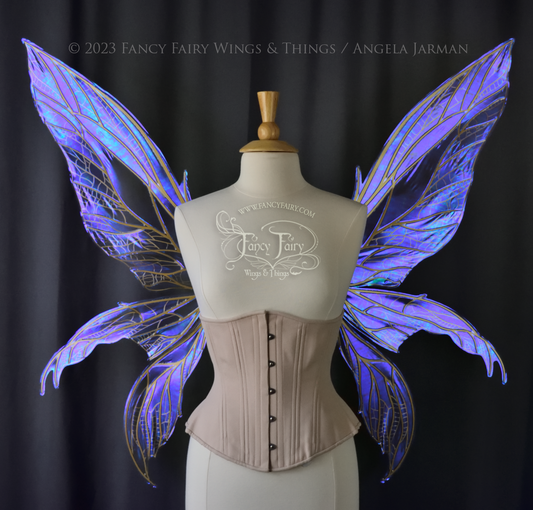 Front view of an ivory dress form wearing an alabaster underbust corset & large violet iridescent fairy wings. Upper panels are elongated with pointed tips, 2 lower panels curve downward, lots of thin vein detail in gold, dark grey background