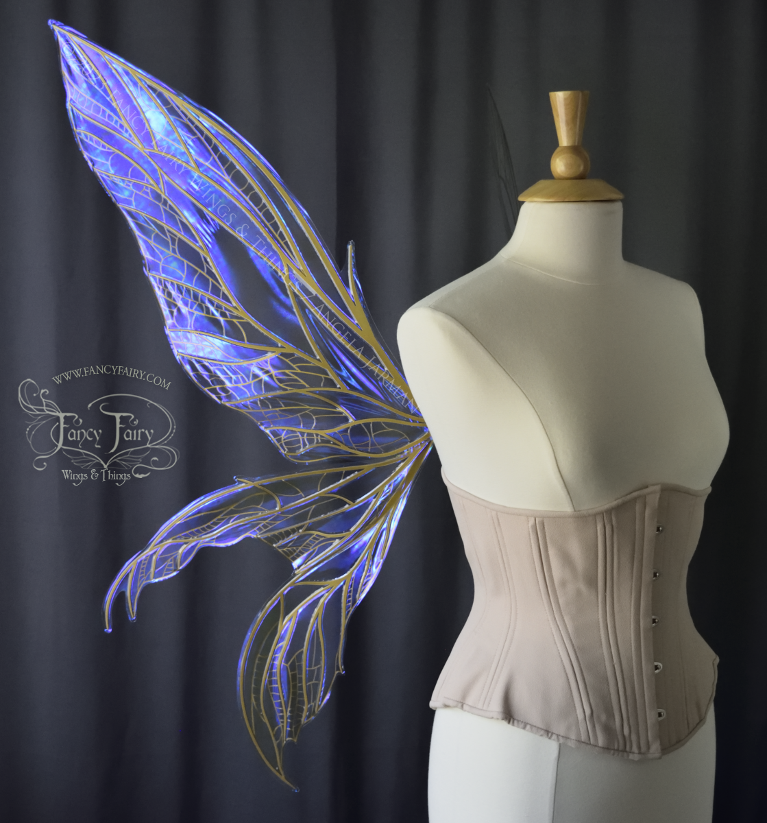 Left side view of an ivory dress form wearing an alabaster underbust corset & large violet iridescent fairy wings. Upper panels are elongated with pointed tips, 2 lower panels curve downward, lots of thin vein detail in gold, dark grey background