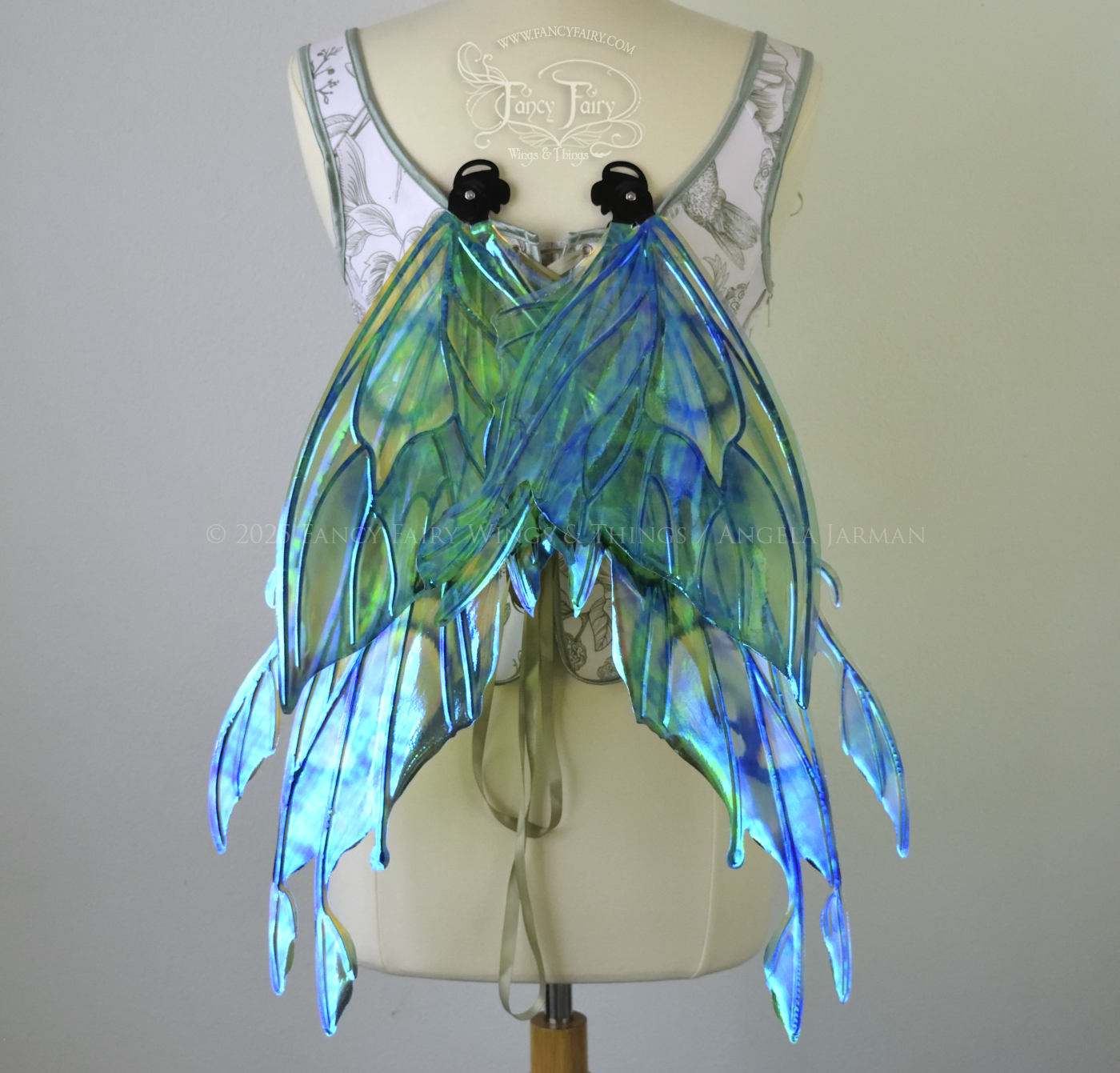 Iridescent green, blue and black fairy wings with antennae and small appendages sticking out from the tips, worn on a dress form, back view, in resting position
