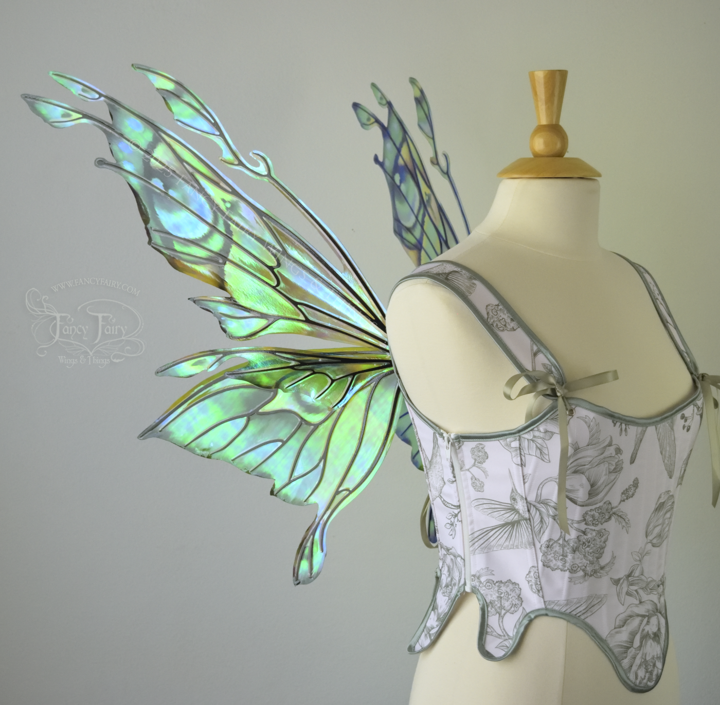 Iridescent green, blue and black fairy wings with antennae and small appendages sticking out from the tips, worn on a dress form, left side view