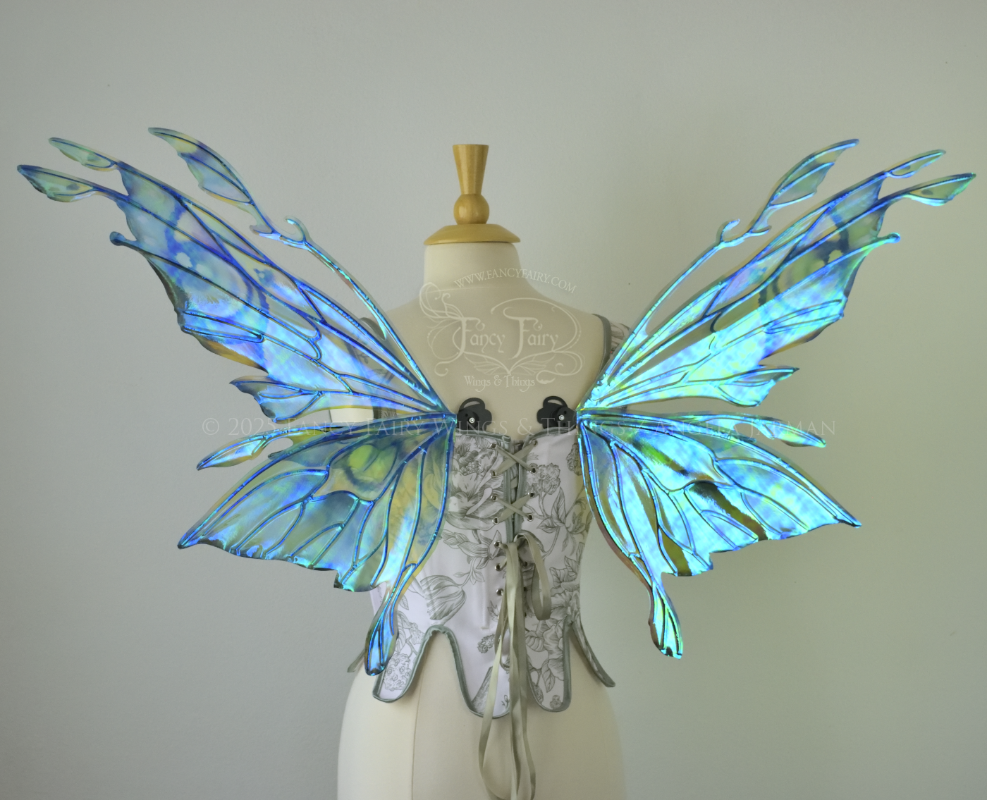 Iridescent green, blue and black fairy wings with antennae and small appendages sticking out from the tips, worn on a dress form, back view