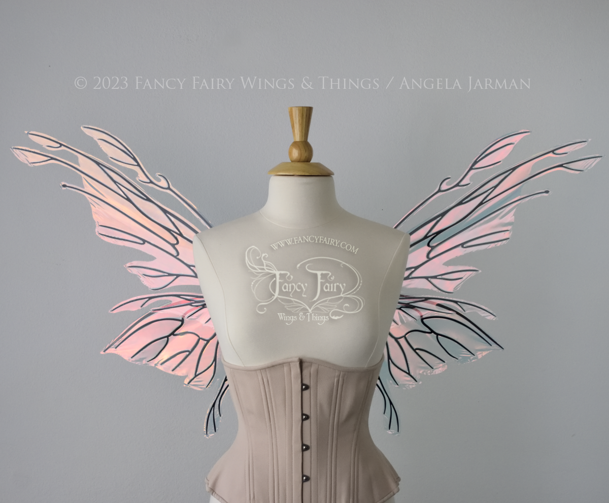 Front view of an ivory dress form wearing an alabaster underbust corset & large blush pink iridescent fairy wings with elongated upper panels with petal like appendages at the tips & antennae, the veins are black