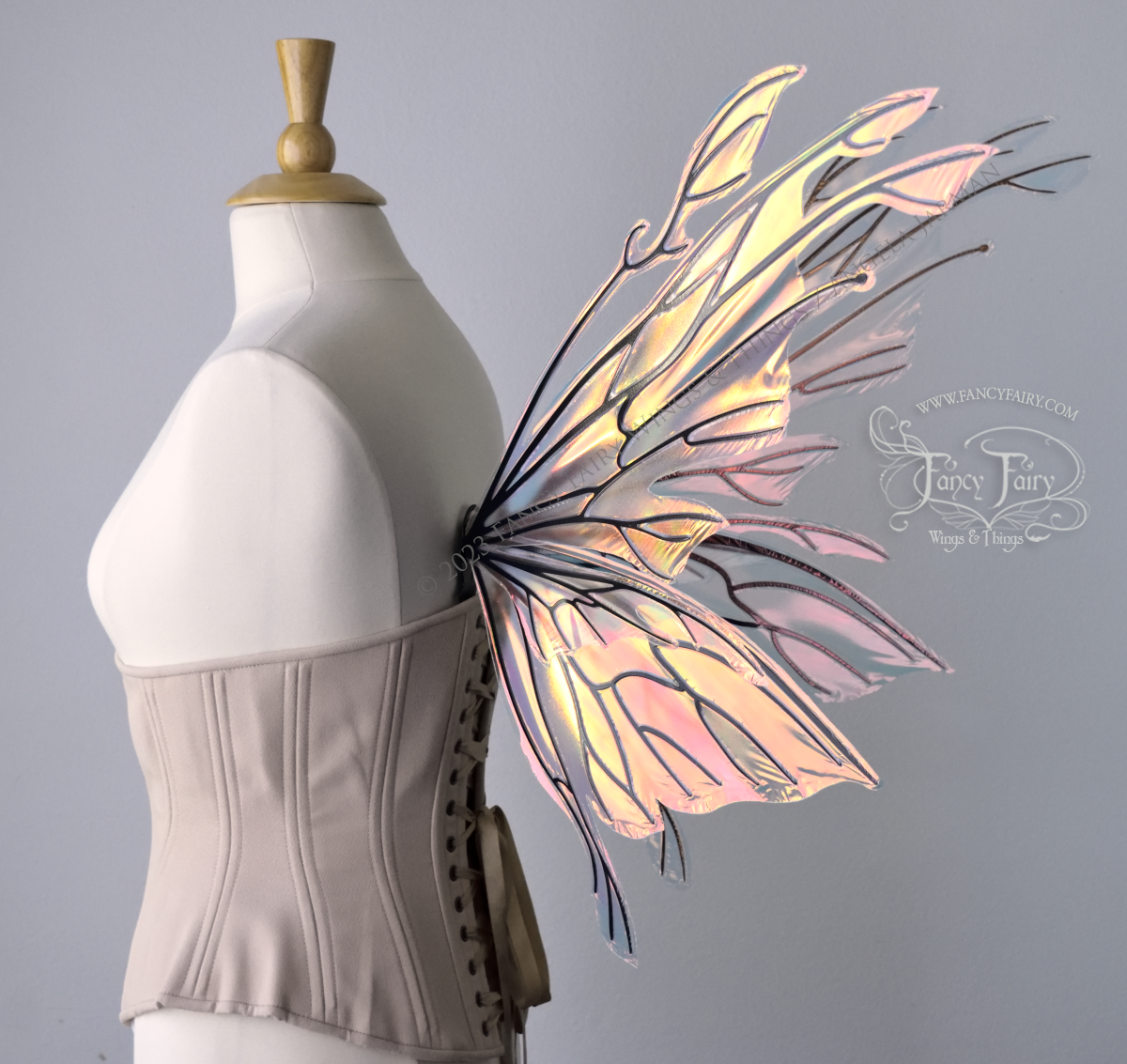 Right 3/4 side view of an ivory dress form wearing an alabaster underbust corset & large blush pink iridescent fairy wings with elongated upper panels with petal like appendages at the tips & antennae, the veins are black