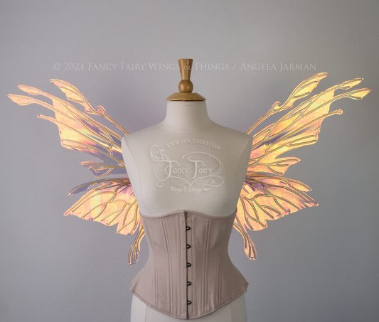Front view of an ivory dress form wearing an alabaster underbust corset & large pink & orange iridescent fairy wings with elongated upper panels with petal like appendages at the tips & antennae, the veins are gold