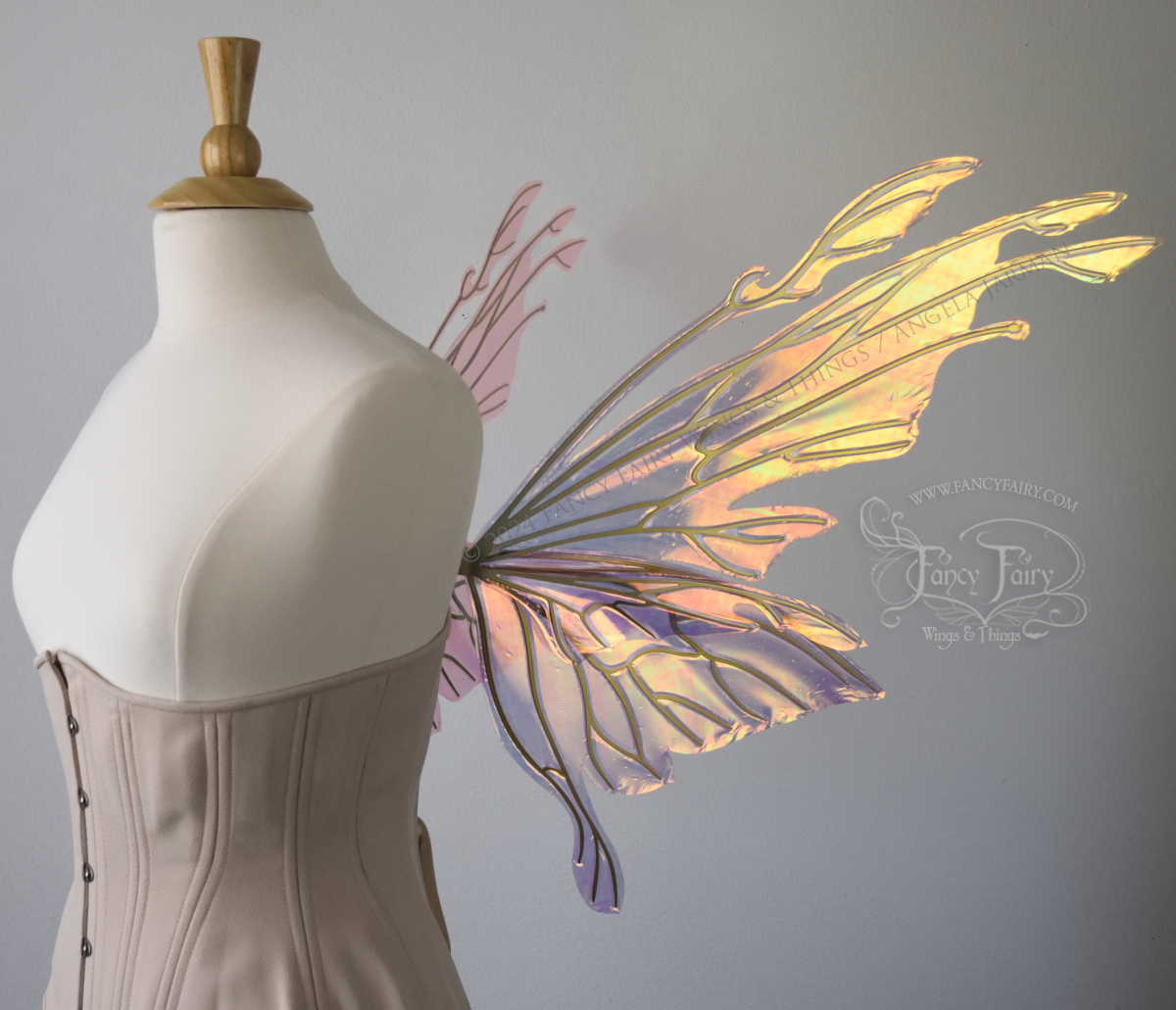 Right side view of an ivory dress form wearing an alabaster underbust corset & large pink & orange iridescent fairy wings with elongated upper panels with petal like appendages at the tips & antennae, the veins are gold