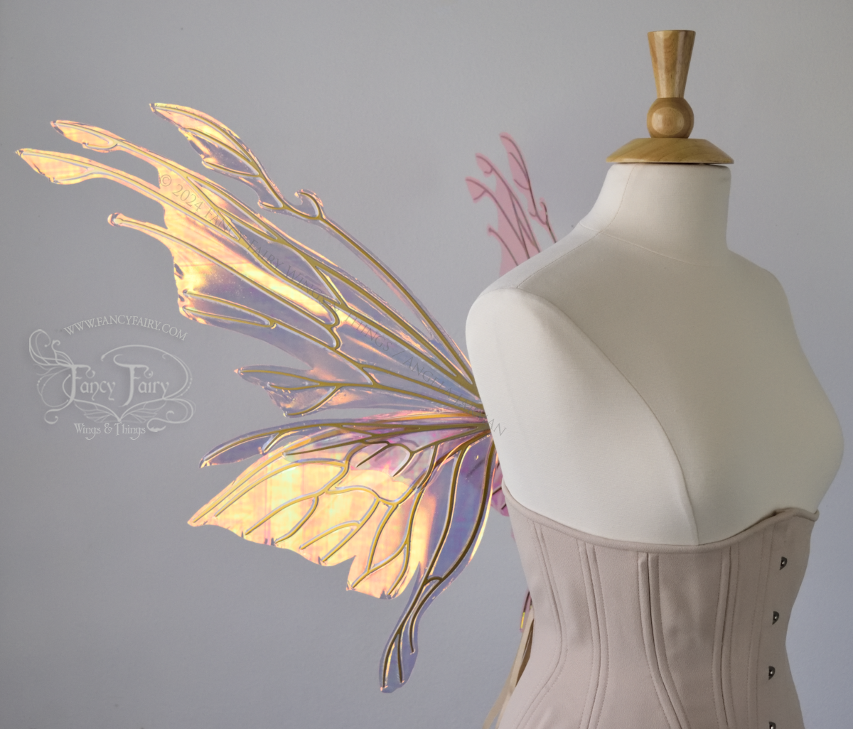 Left side view of an ivory dress form wearing an alabaster underbust corset & large pink & orange iridescent fairy wings with elongated upper panels with petal like appendages at the tips & antennae, the veins are gold