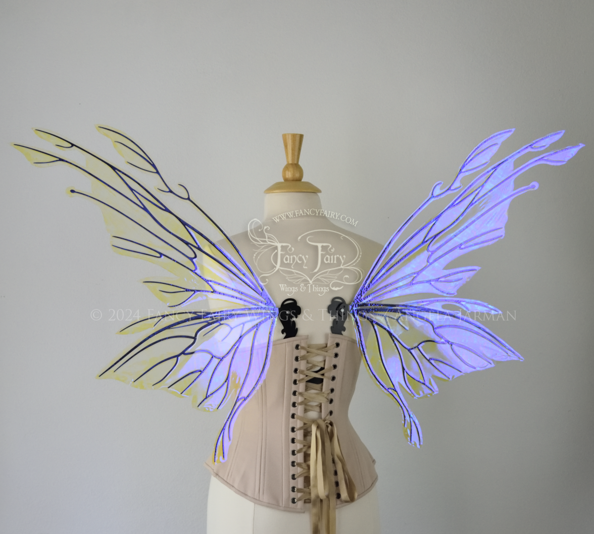 Back view of an ivory dress form wearing an alabaster underbust corset & large violet iridescent fairy wings with elongated upper panels with petal like appendages at the tips & antennae, the veins are black